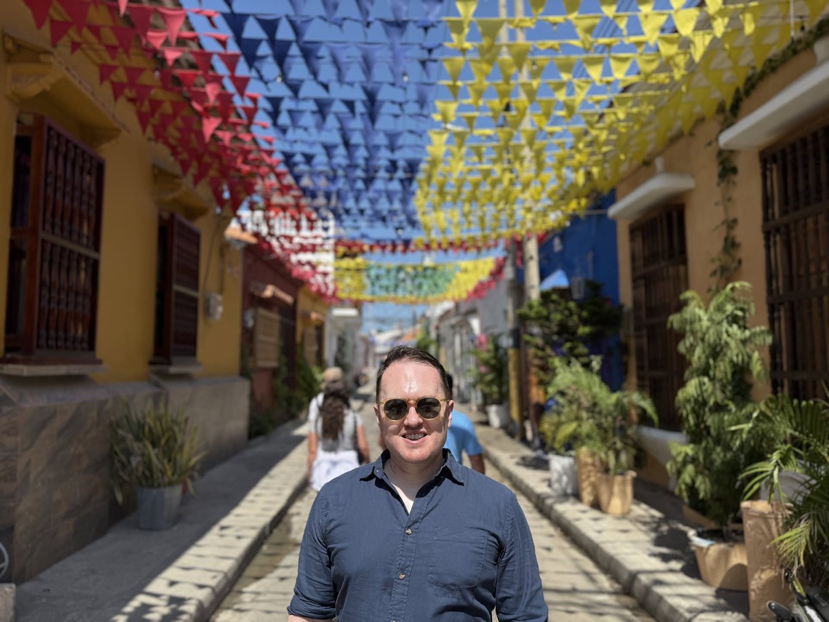 In sunglasses beneath a canopy of red, blue, and yellow pennants strung over an old-town street