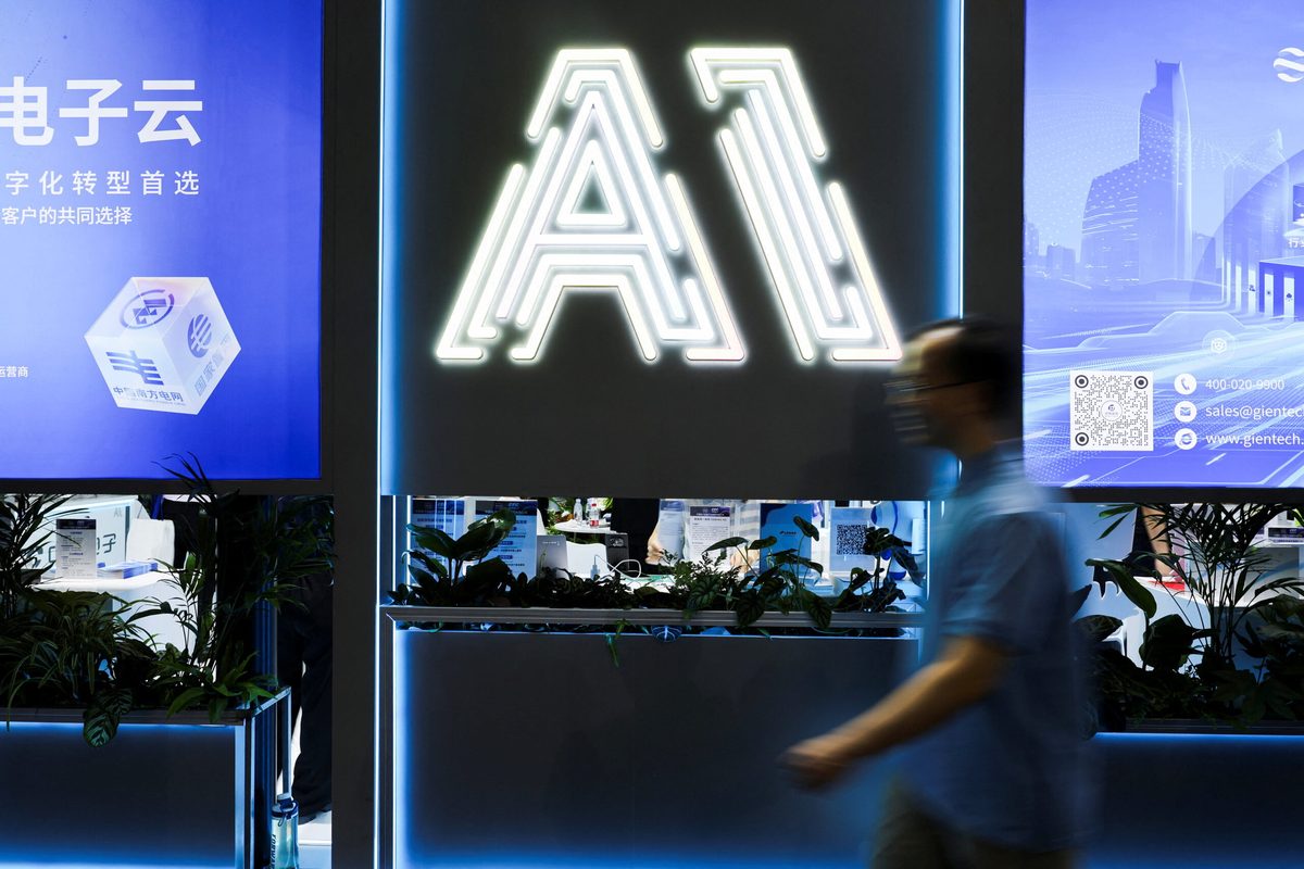 News photograph: a figure walking past an illuminated “AI” sign and banks of video panels at a Chinese technology expo.