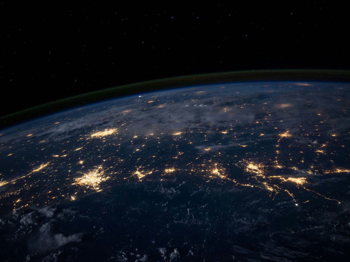 NASA photograph of Earth from orbit at night: city lights strung across a dark landmass under the curve of the atmosphere.