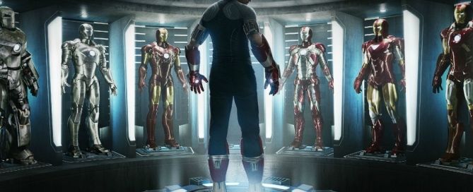 Film still of Tony Stark standing in a room lined with multiple Iron Man suits of armor.