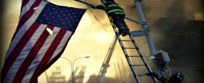 A firefighter on a ladder holding an American flag amid smoke and wreckage at the World Trade Center site.
